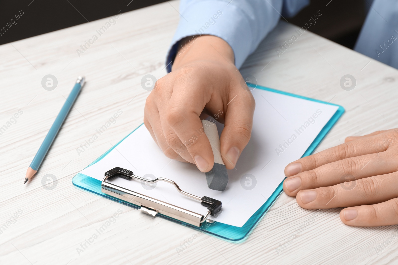 Photo of Man erasing something on paper at white wooden table, closeup