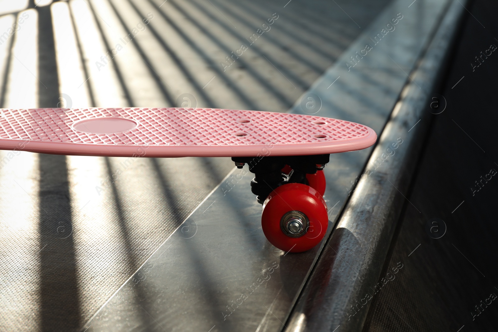 Photo of Modern pink skateboard with red wheels on top of ramp outdoors, closeup