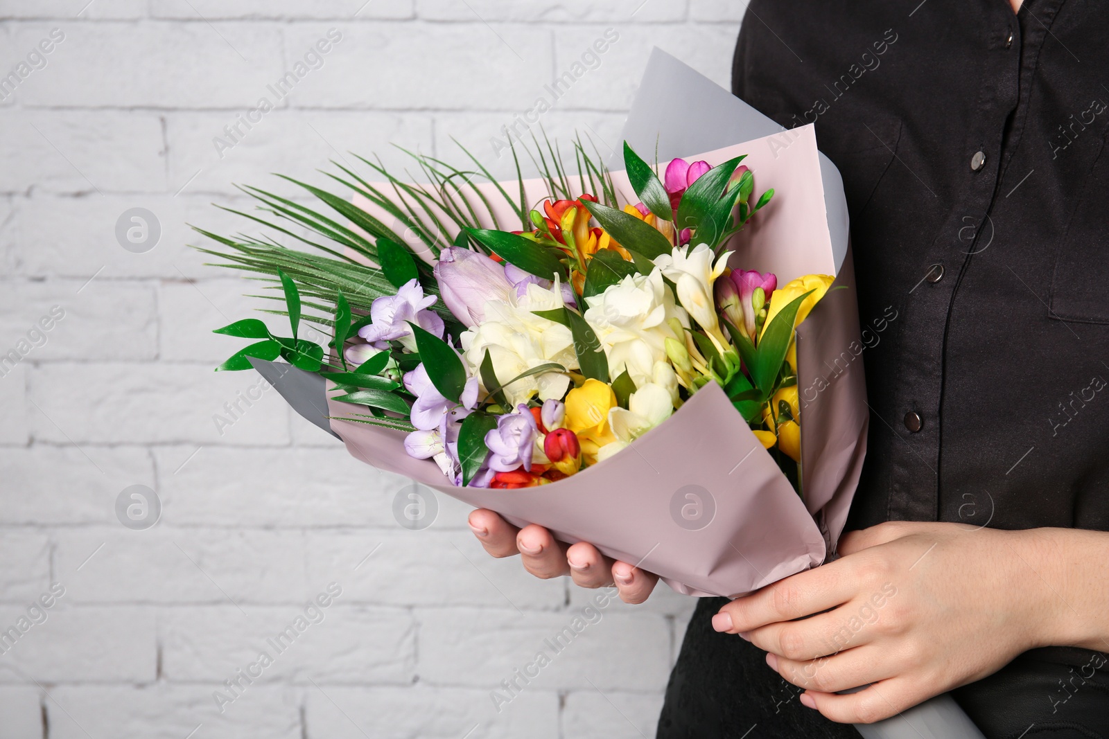 Photo of Woman with beautiful bouquet of freesia flowers on brick wall background