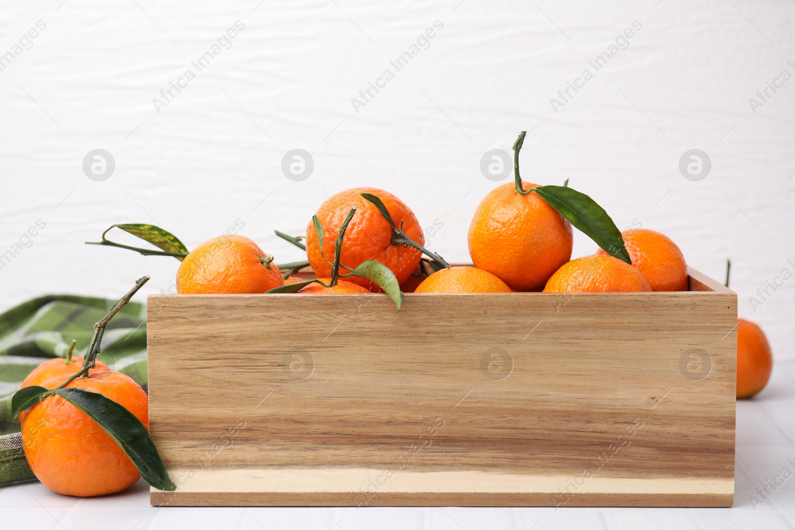 Photo of Wooden crate with fresh ripe tangerines and leaves on white table