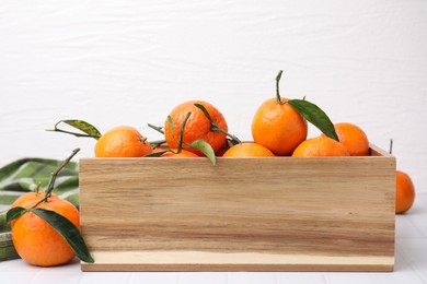 Photo of Wooden crate with fresh ripe tangerines and leaves on white table