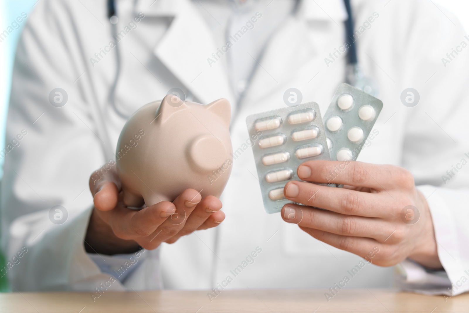 Photo of Doctor with piggy bank and pills at table, closeup