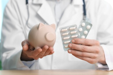 Photo of Doctor with piggy bank and pills at table, closeup