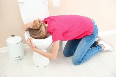 Photo of Young woman vomiting in toilet bowl at home