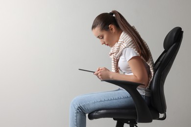 Photo of Young woman with poor posture using tablet while sitting on chair against grey background, space for text