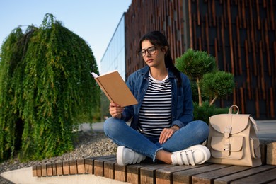 Photo of Young woman reading book on bench outdoors