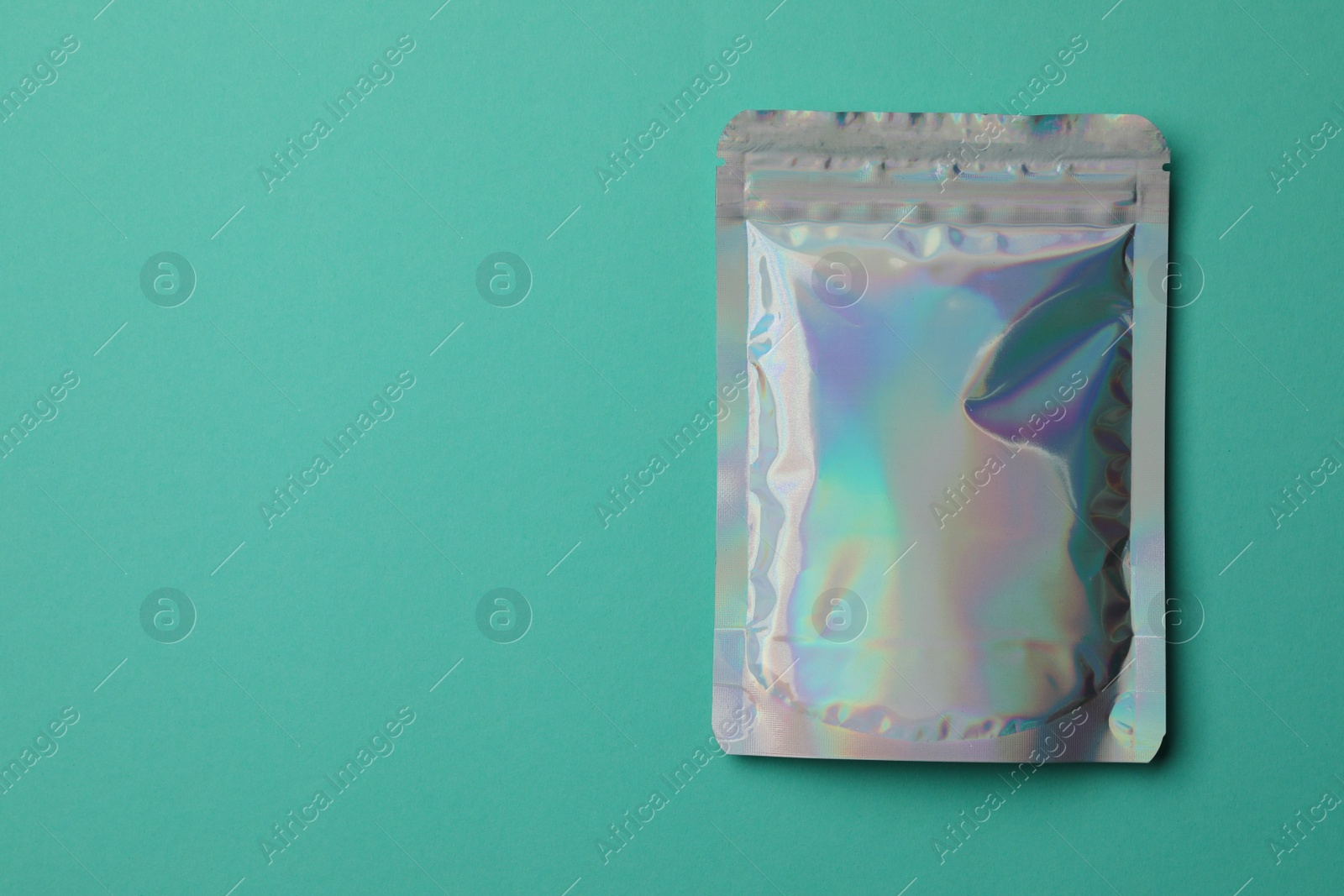 Photo of Blank foil package on turquoise background, top view. Space for text