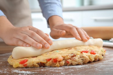 Photo of Woman putting marzipan into raw dough for Stollen at wooden table, closeup. Baking traditional German Christmas bread
