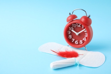 Photo of Different feminine hygiene products with red feather and alarm clock on color background, space for text. Gynecological care