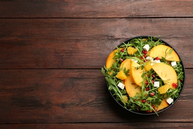 Photo of Delicious persimmon salad with pomegranate and arugula on wooden table, top view. Space for text