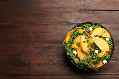 Delicious persimmon salad with pomegranate and arugula on wooden table, top view. Space for text