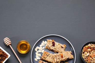 Photo of Tasty granola bars and ingredients on grey wooden table, flat lay. Space for text