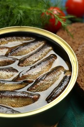 Tin can with tasty sprats on table, closeup