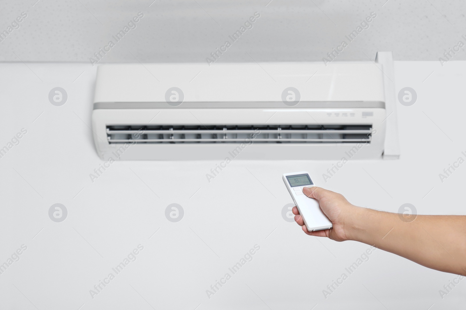 Photo of Man operating air conditioner with remote control indoors, closeup