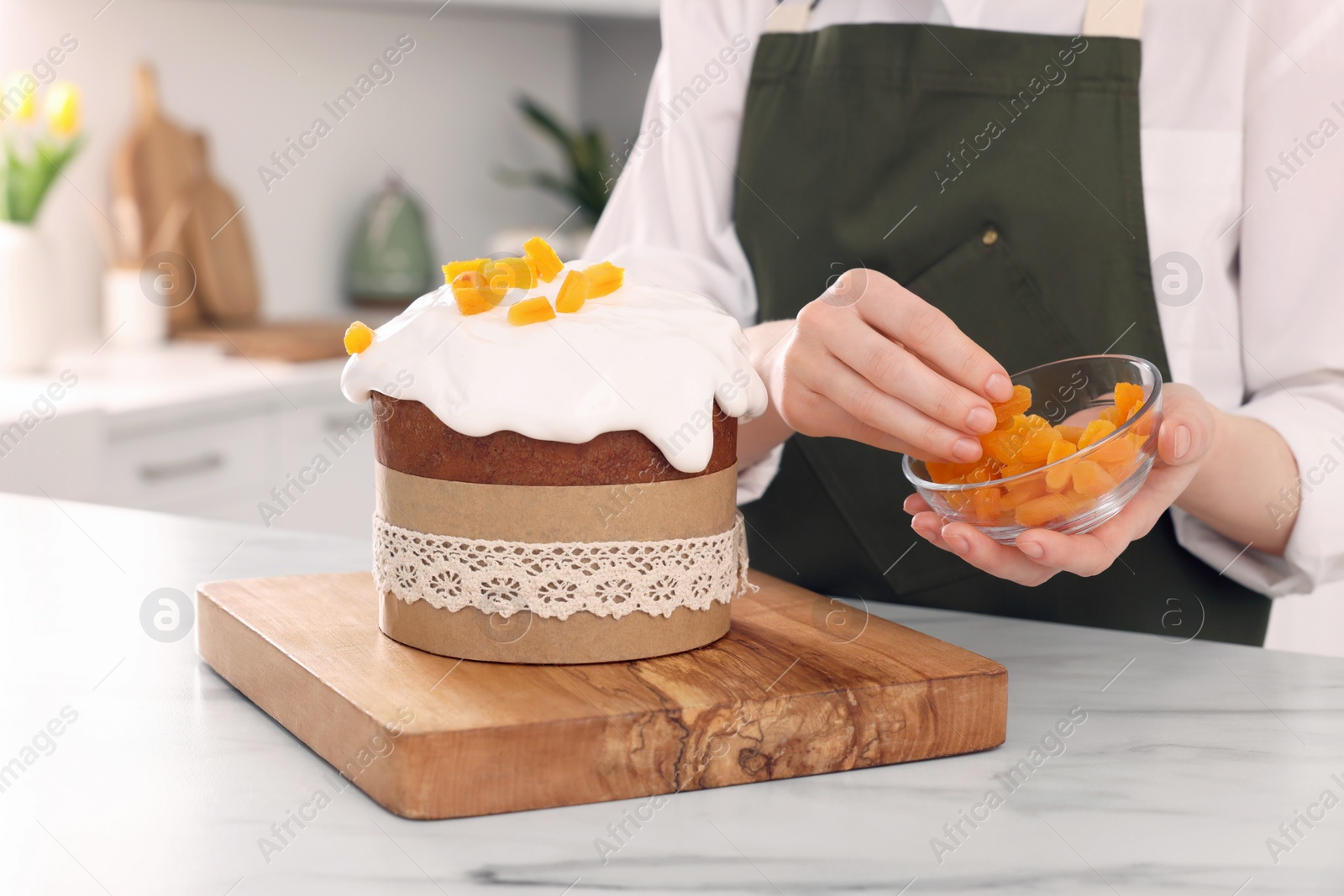 Photo of Woman decorating delicious Easter cake with dried apricots at white marble table in kitchen, closeup