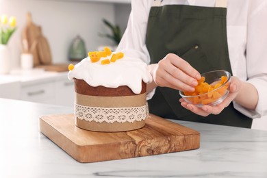 Woman decorating delicious Easter cake with dried apricots at white marble table in kitchen, closeup