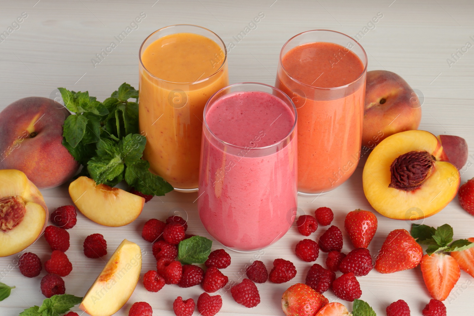 Photo of Fresh colorful fruit smoothies and ingredients on white wooden table