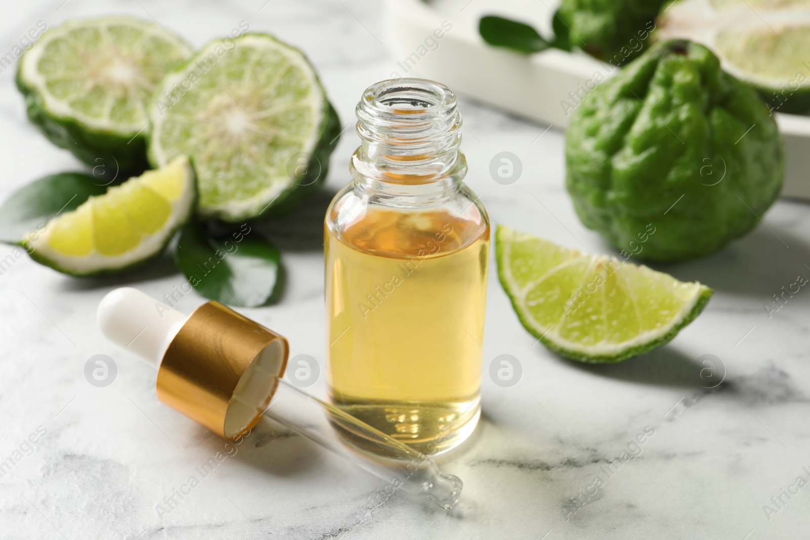 Photo of Bottle of essential oil, pipette and fresh bergamot fruits on white marble table