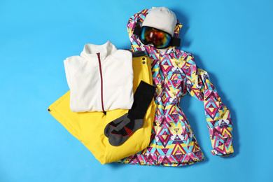 Stylish winter sport clothes on light blue background, flat lay