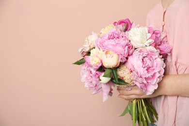 Woman with bouquet of beautiful peonies on beige background, closeup. Space for text
