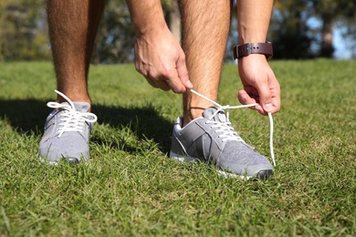 Sporty man tying shoelaces in park on sunny morning, closeup