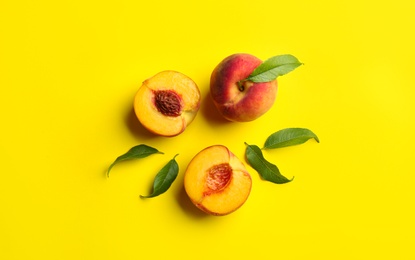 Photo of Fresh ripe peaches and green leaves on yellow background, flat lay