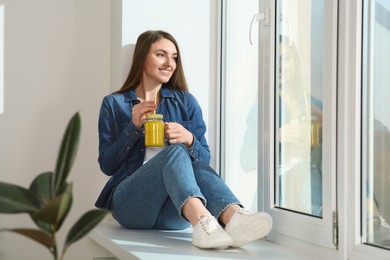Photo of Beautiful young woman with delicious smoothie near window. Space for text