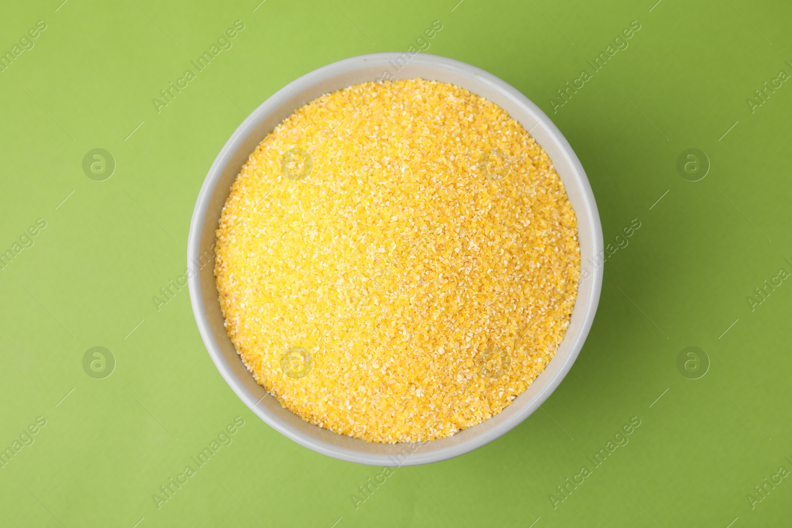 Photo of Raw cornmeal in bowl on green table, top view