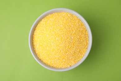 Photo of Raw cornmeal in bowl on green table, top view