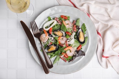 Plate of delicious salad with seafood on white tiled table, flat lay