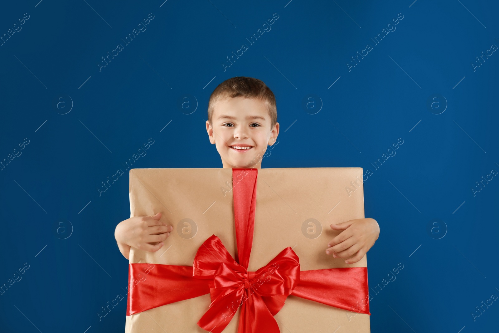 Image of Cute little boy dressed as gift box on blue background. Christmas suit