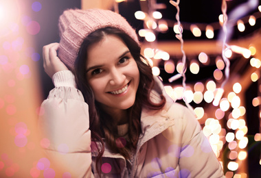 Image of Beautiful young woman near festive lights outdoors. Winter vacation