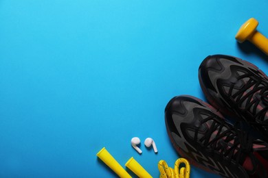 Photo of Sneakers, skipping rope and dumbbell on light blue background, flat lay with space for text. Morning exercise