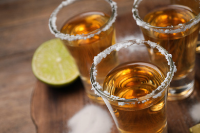 Photo of Mexican Tequila shots, lime and salt on wooden table, closeup