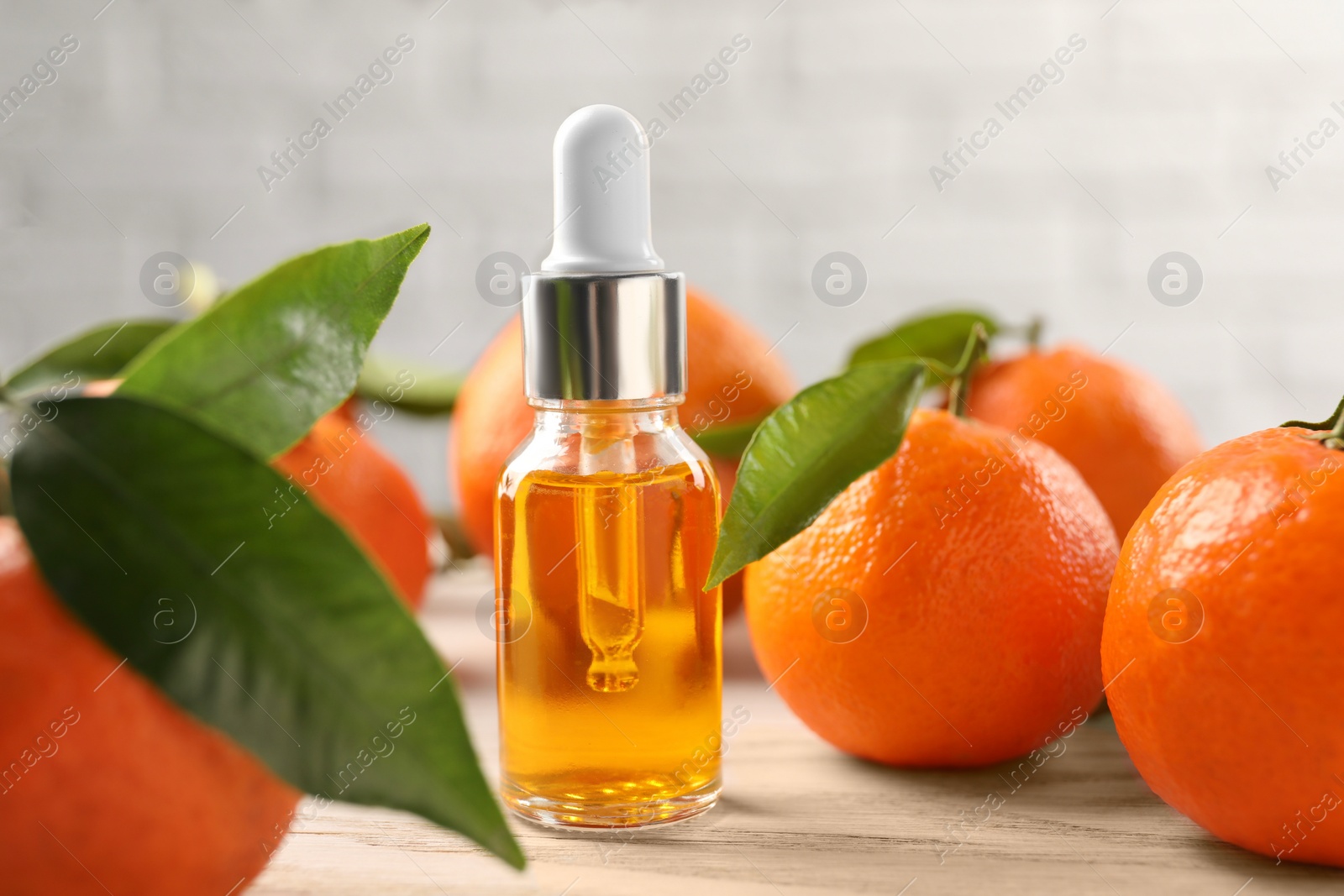 Photo of Bottle of tangerine essential oil and fresh fruits on white wooden table, closeup