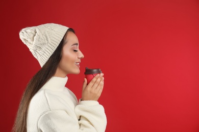 Photo of Happy beautiful woman with paper cup of mulled wine on red background. Space for text