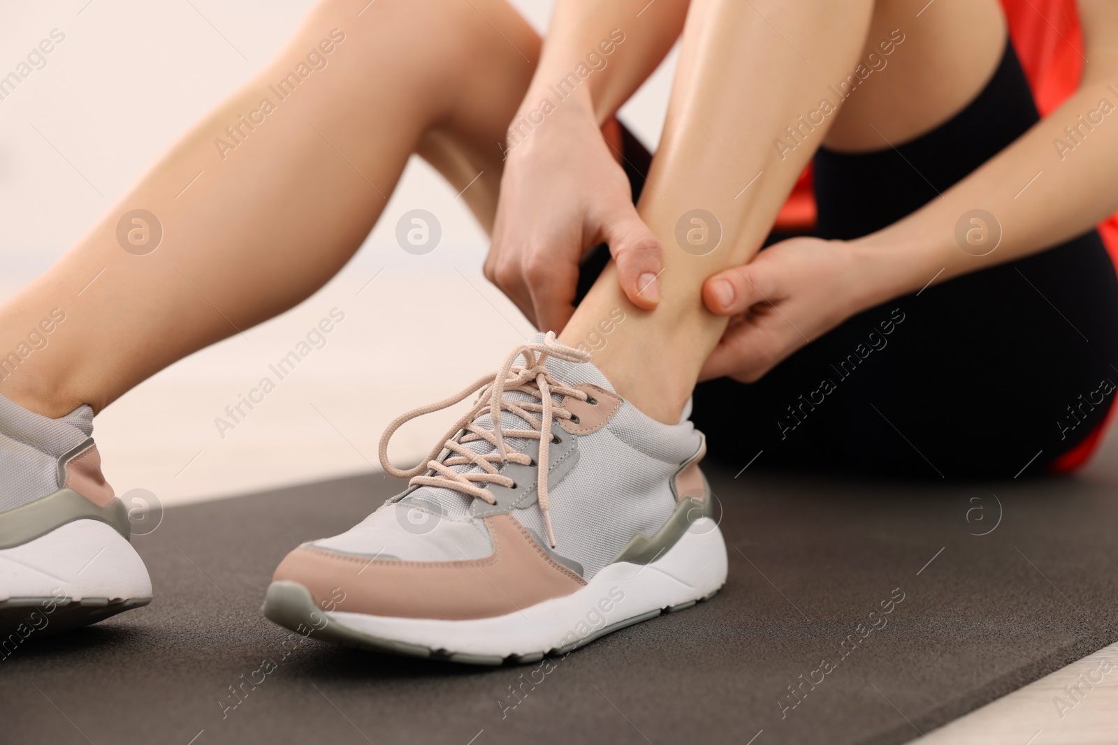 Photo of Woman suffering from leg pain on exercise mat indoors, closeup