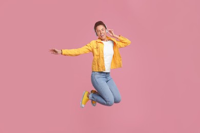 Photo of Happy young woman in headphones jumping while dancing on pink background