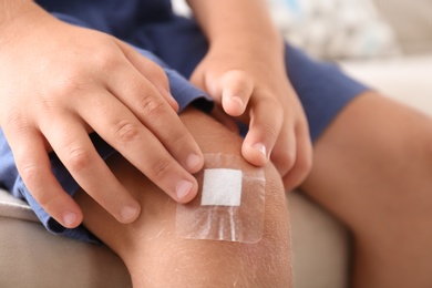 Photo of Little boy with adhesive bandage on knee indoors, closeup