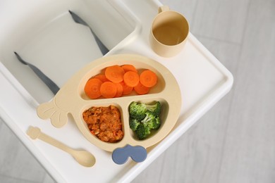 Photo of High chair baby tableware on white tray indoors, top view