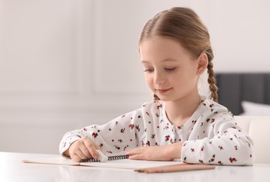 Girl using eraser at white desk indoors. Space for text