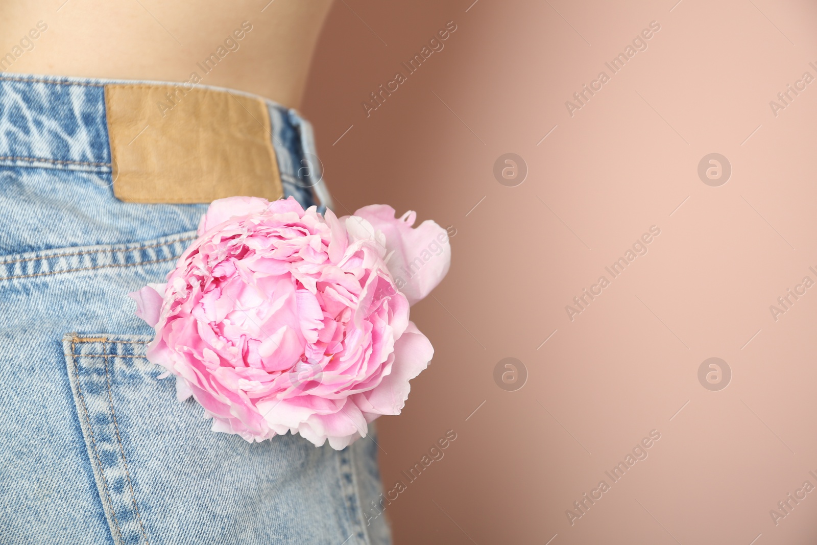 Photo of Woman with pink peony in pocket on beige background, closeup. Space for text