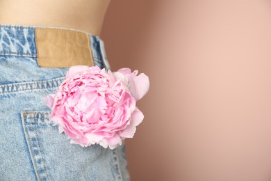 Photo of Woman with pink peony in pocket on beige background, closeup. Space for text