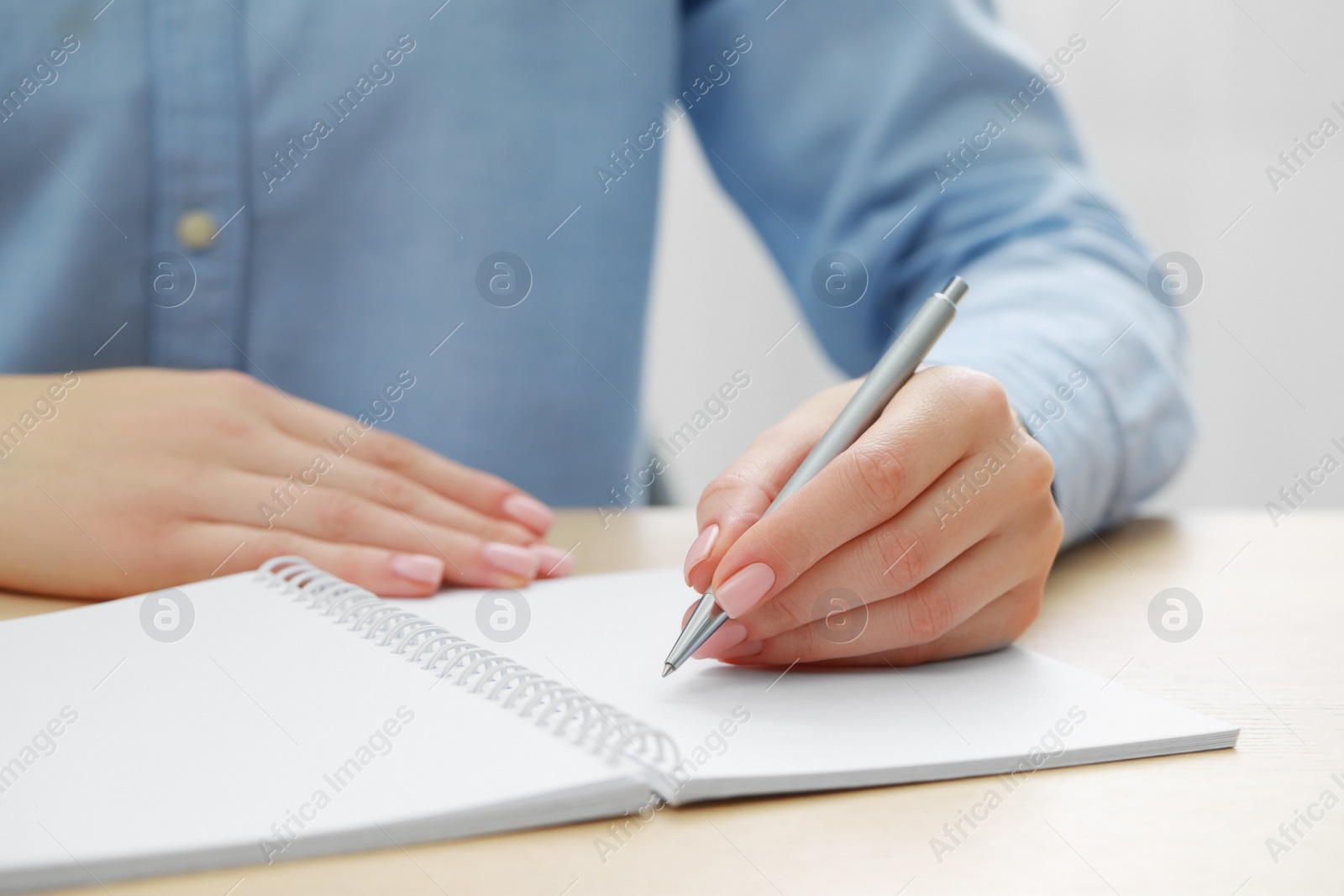 Photo of Woman writing in notebook at wooden table, closeup