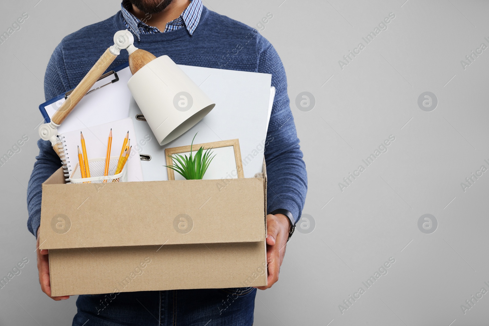 Photo of Unemployed man with box of personal office belongings on light grey background, closeup. Space for text