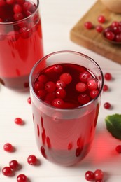 Tasty cranberry juice in glasses and fresh berries on white wooden table, closeup