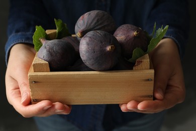 Photo of Woman holding wooden crate with tasty raw figs on grey background, closeup