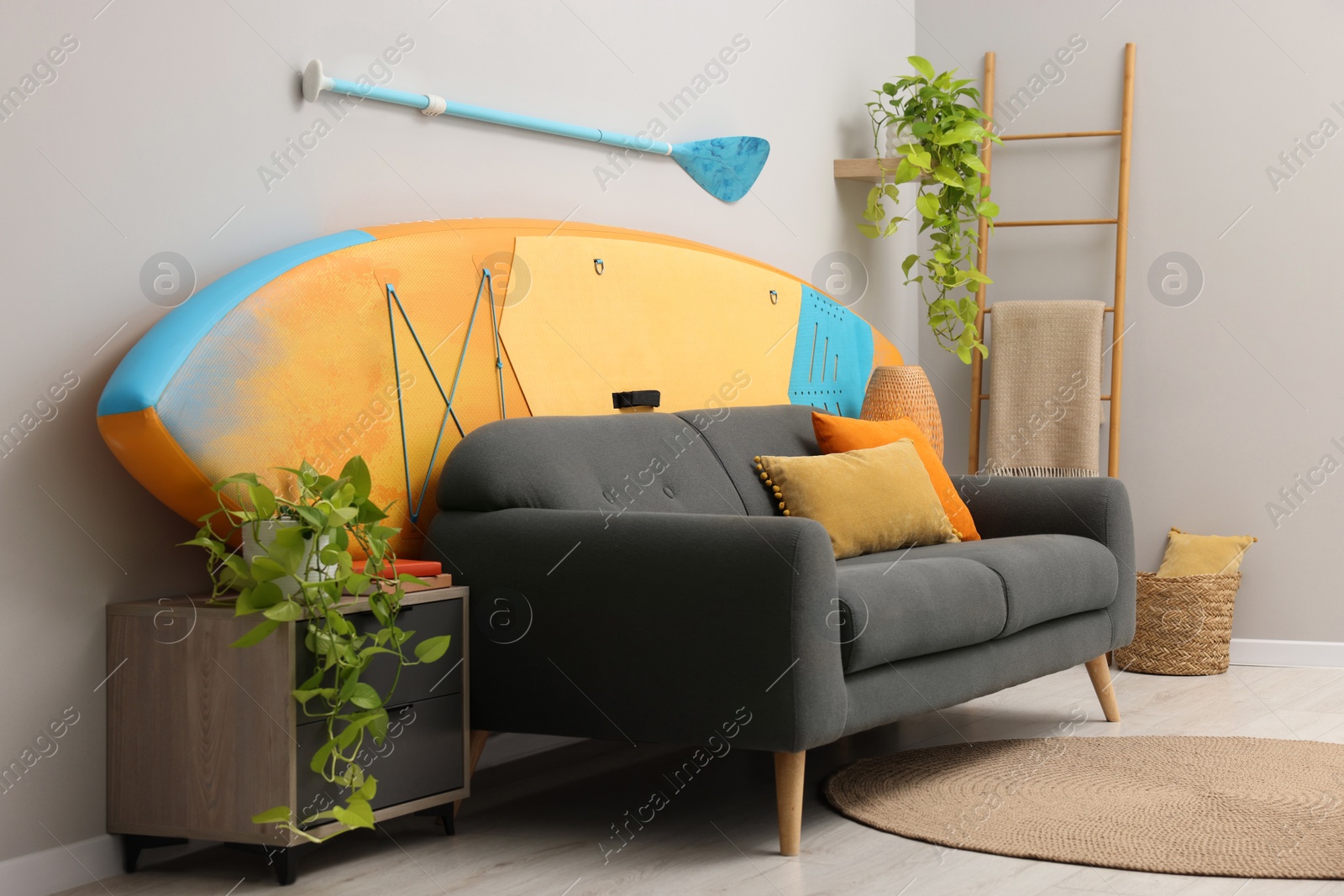 Photo of SUP board, paddle and stylish sofa in living room. Interior design