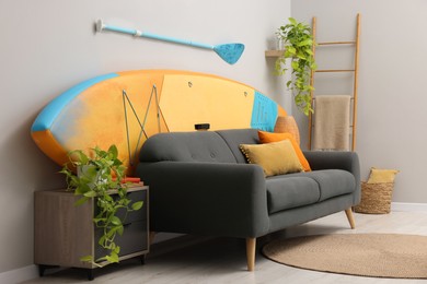 SUP board, paddle and stylish sofa in living room. Interior design