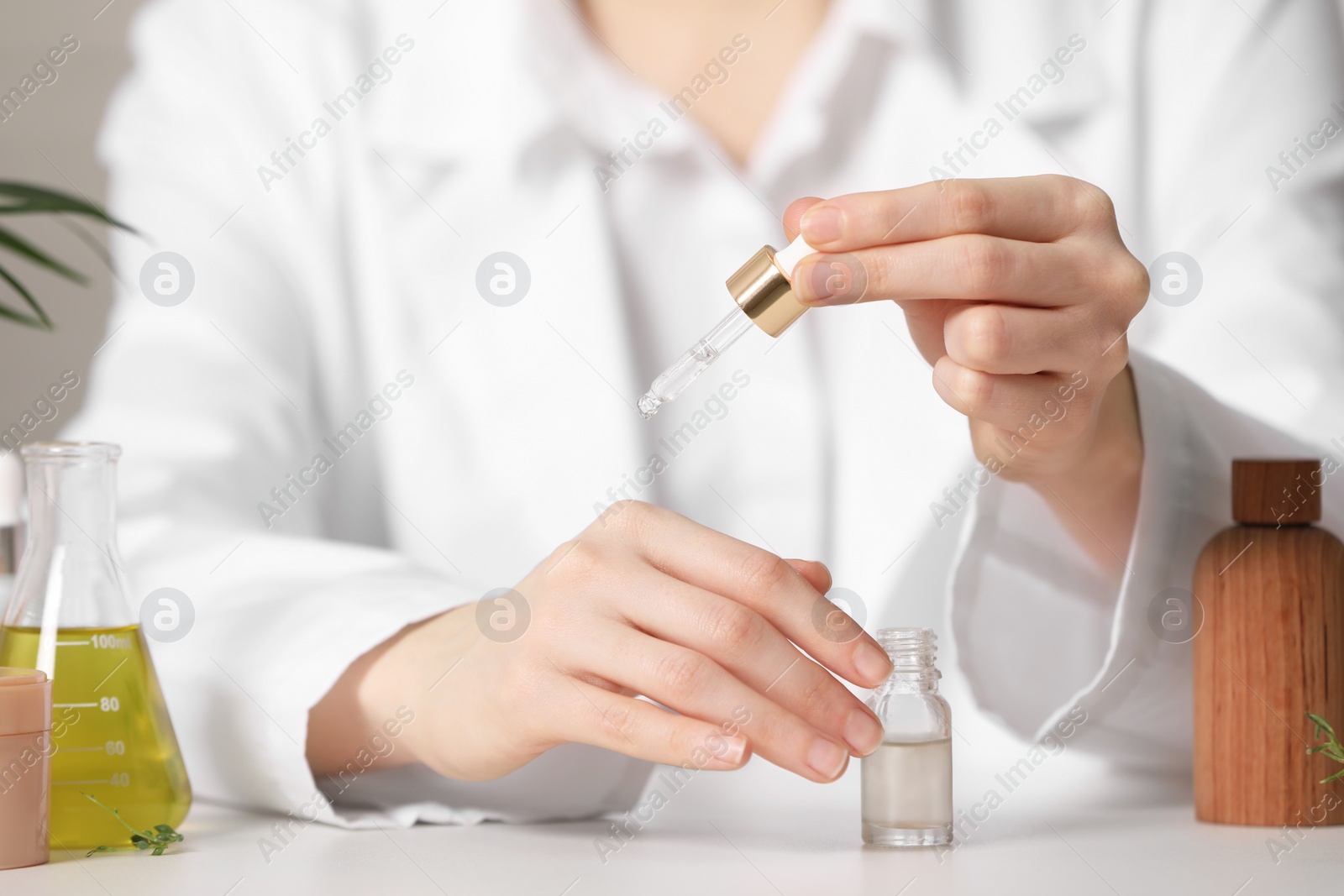 Photo of Dermatologist testing essential oil at white table indoors, selective focus